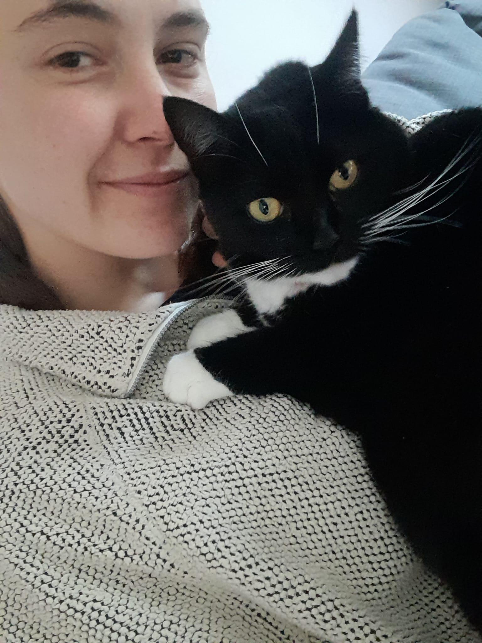A selfie of a young woman cuddling a black and white cat